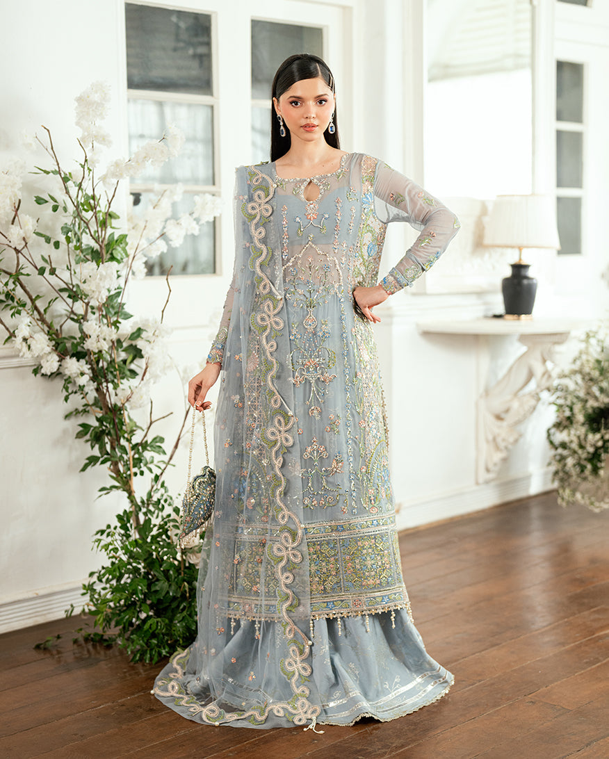 Woman wearing pastel blue embroidered chiffon dress with floral sequined designs and holding matching embellished handbag