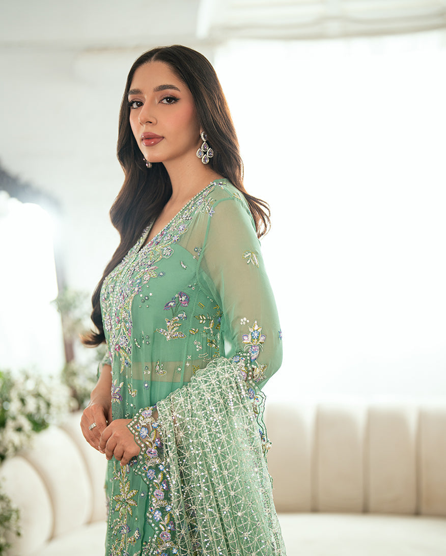 Close-up view of the embroidered neckline with sequins, pearls, and floral threadwork on green chiffon fabric