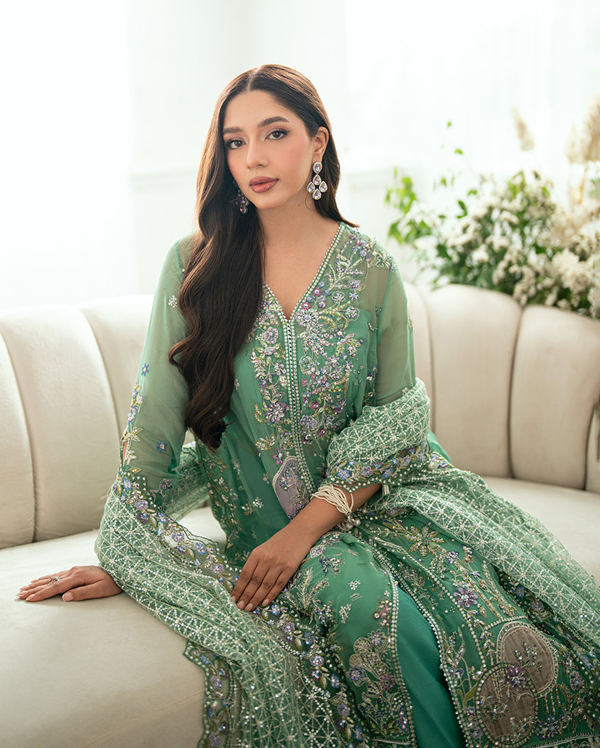 Close-up of woman sitting on a beige sofa in green embroidered chiffon suit with intricate beadwork and floral embroidery on the neckline