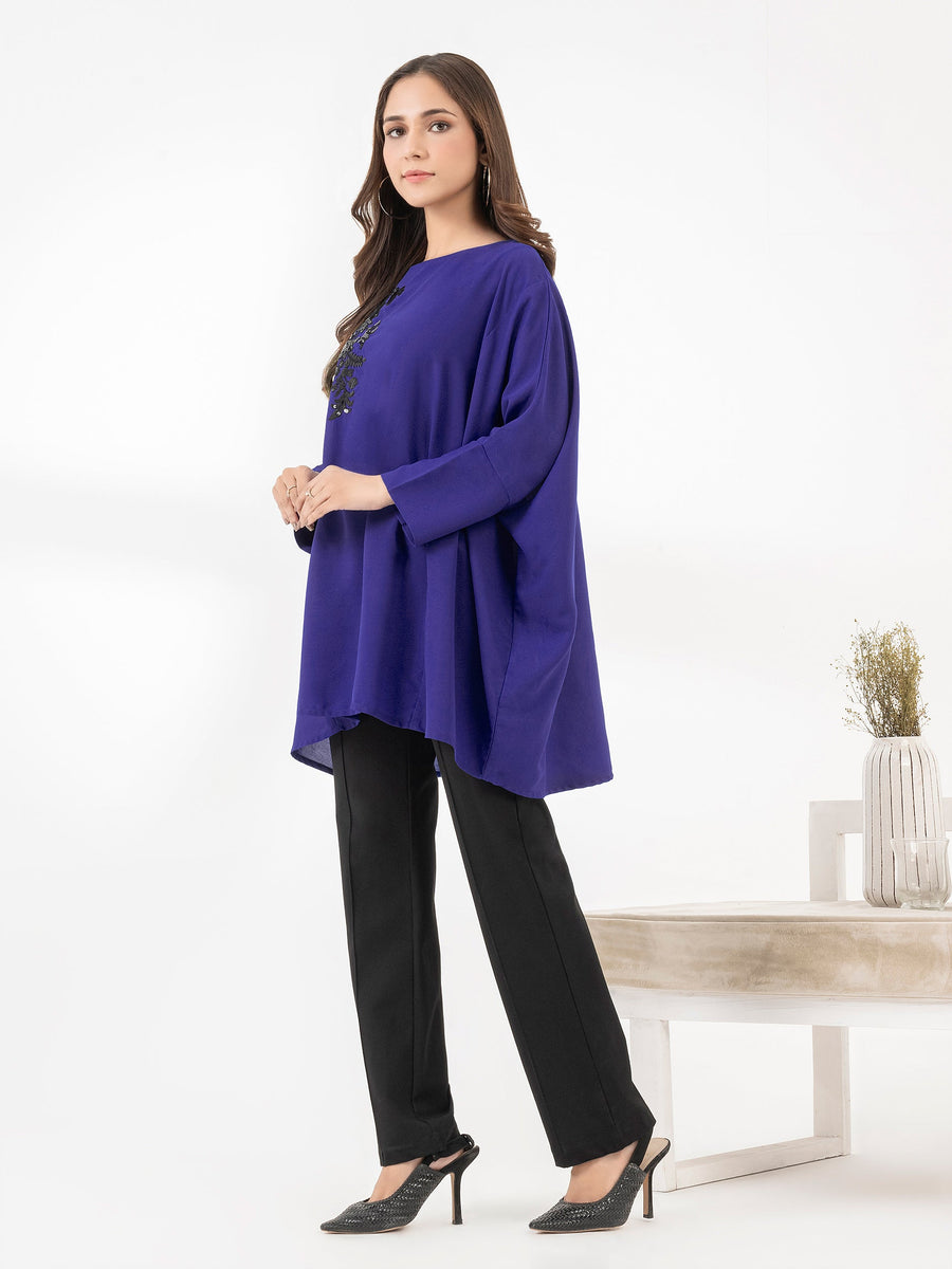 Side view of woman modeling royal blue embroidered loose fit top paired with black pants and stylish heels