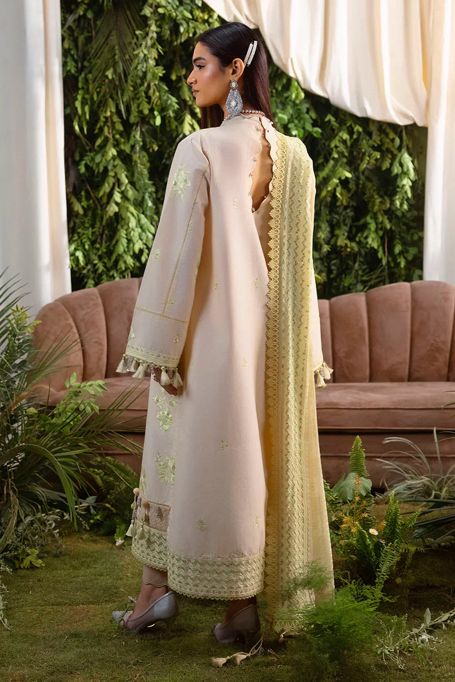 Full length side view of woman in pastel cream embroidered lawn suit with chiffon dupatta, highlighted tassel accents, and elegant heels
