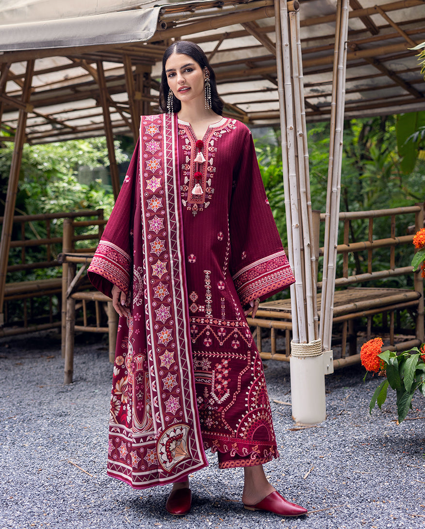 Woman wearing maroon embroidered karandi suit with printed shawl standing in a bamboo garden