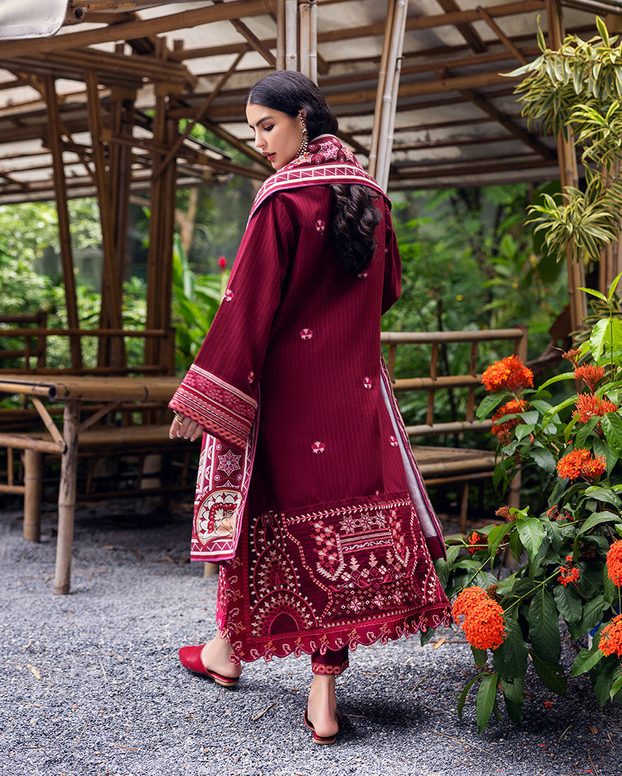 Back view of woman in maroon embroidered karandi suit highlighting embroidery on hem and shawl draped over shoulder