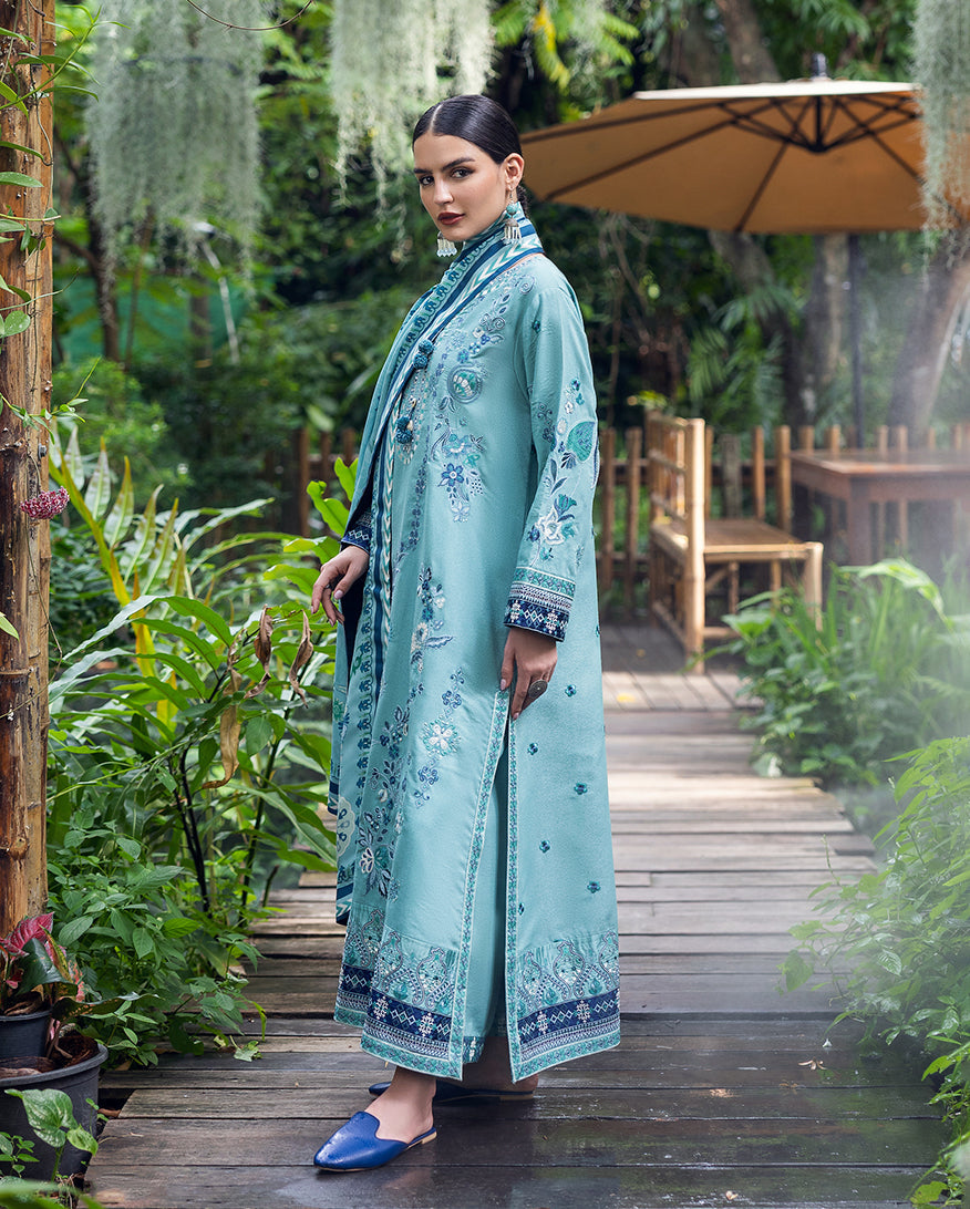 Side view of a woman showcasing the full embroidered long aqua blue karandi shirt with detailed cuffs and side slits paired with matching trousers and blue shoes.