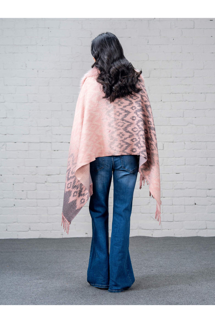 Back view of woman wearing pink wool cape showcasing two-tone woven pattern and fringed hem over blue jeans
