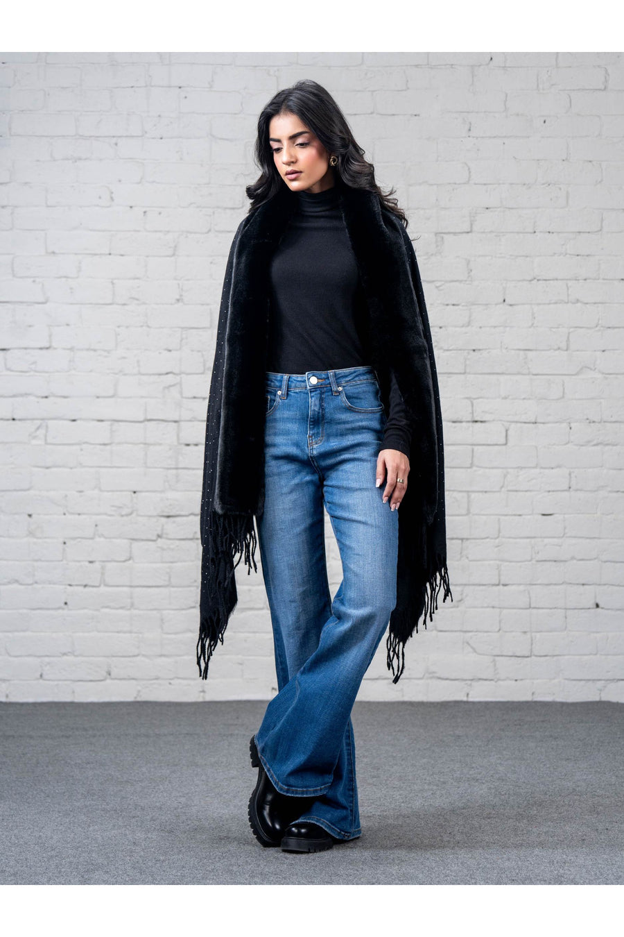 Woman wearing black wool cape shawl draped over shoulders showing front with subtle rhinestone detailing, posed angled with crossed legs