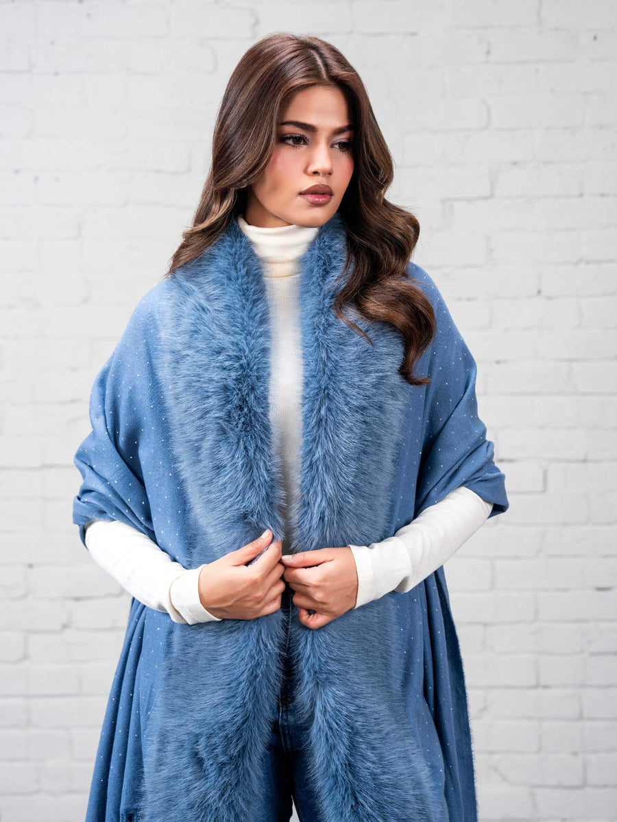 Woman holding the edges of her sky blue wool cape with faux fur trim and fringe, showing texture and elegant drape