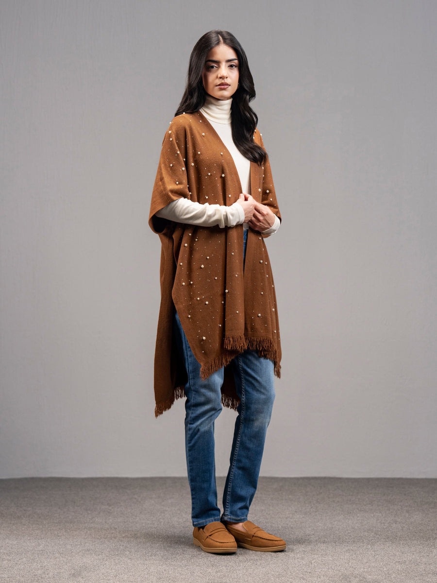 Side-front angle of the same woman showcasing the loose draping and pearl detailing of the rust wool cape over casual attire.