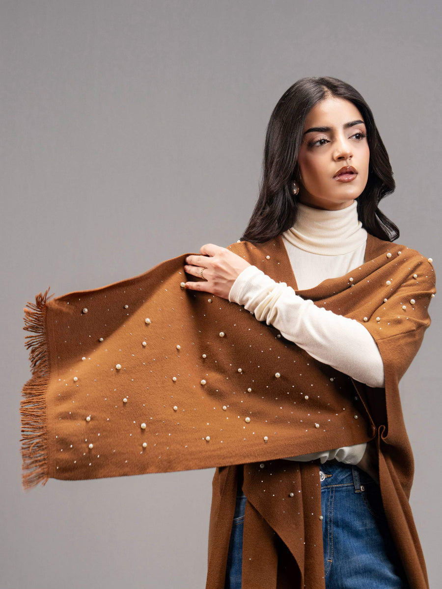 Close-up detail of the pearl and stone embellishments on the rust wool cape fabric highlighted as the woman holds out the cape.