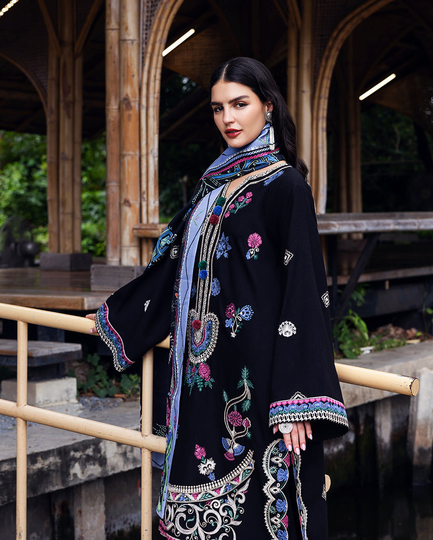 Side view of woman showcasing the intricate embroidery on black Karandi shirt and tassel bordered sleeves with printed shawl