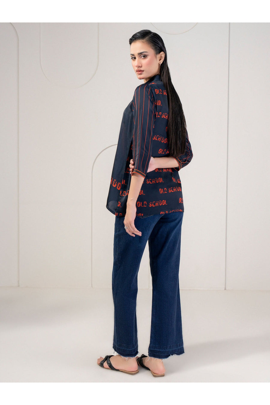 Back view showing navy printed silk top with repeating 'OLD SCHOOL' motif and striped sleeves.