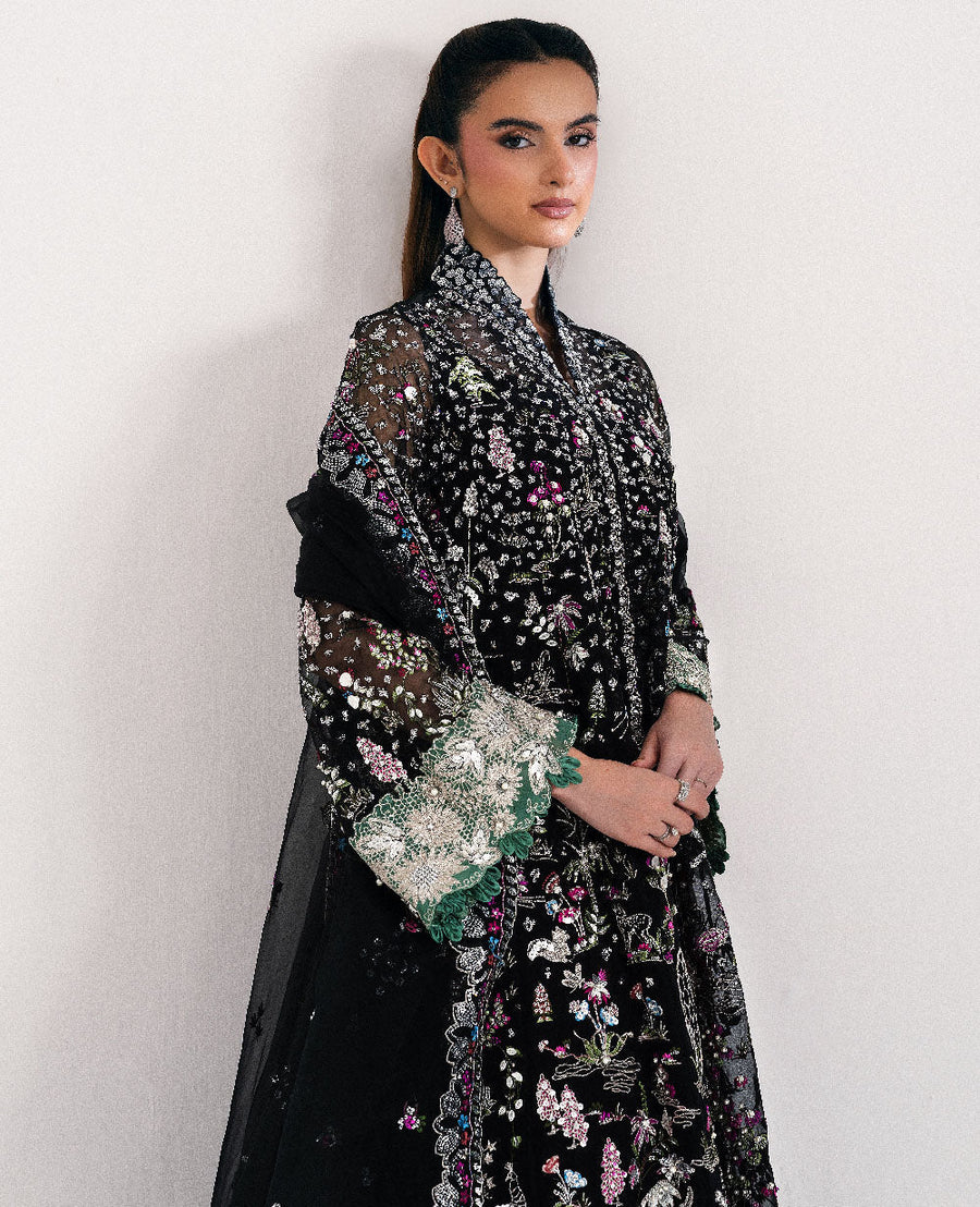 Close-up front view of model in embroidered black organza suit showing delicate colorful floral embroidery and green lace cuffs