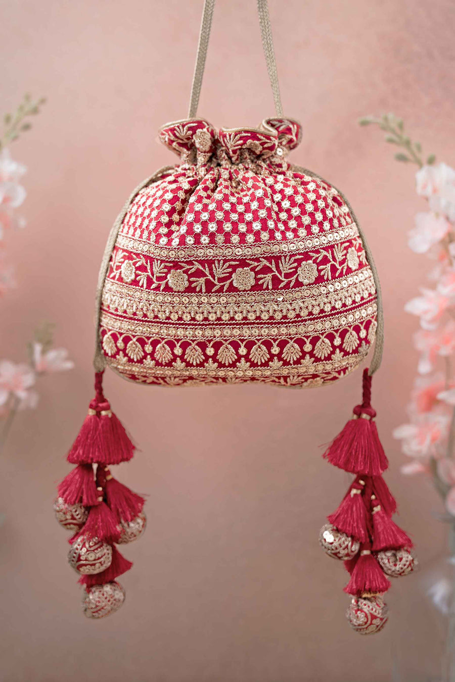 Red potli bag with gold embroidery and tassel details hanging against a soft pink background