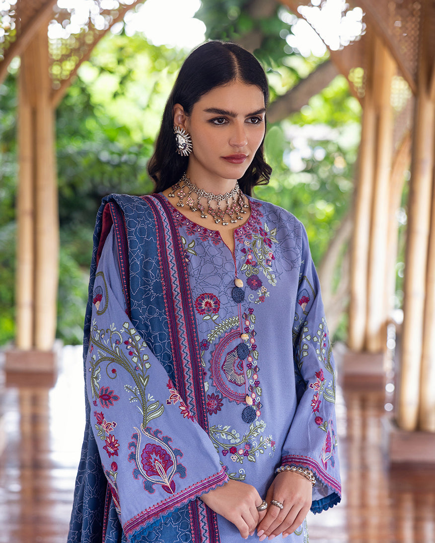 Close-up of a woman in a lavender Karandi suit showing detailed floral embroidery on the front and sleeves with decorative buttons, accessorized with silver jewelry.