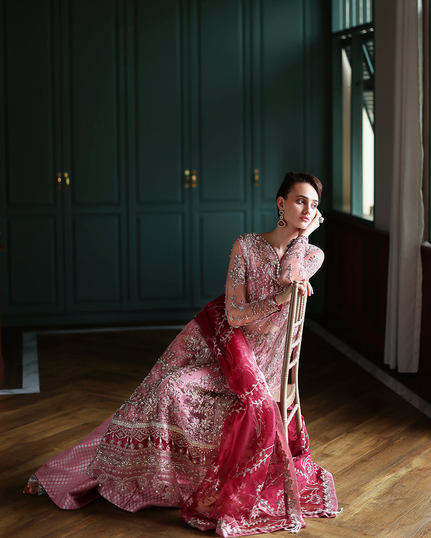 Model seated on chair wearing pink embroidered dress with deep rose dupatta, highlighting the dress’s flowing fabric and detailed embroidery