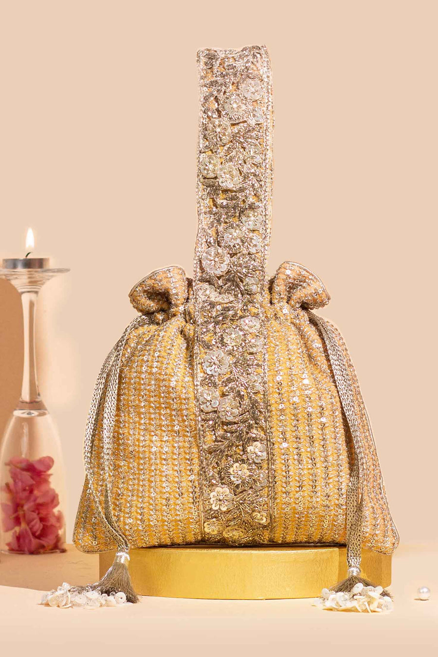 Gold potli bag with detailed floral embroidery, shimmering sequins, tassel drawstrings, and an embellished handle on a beige background