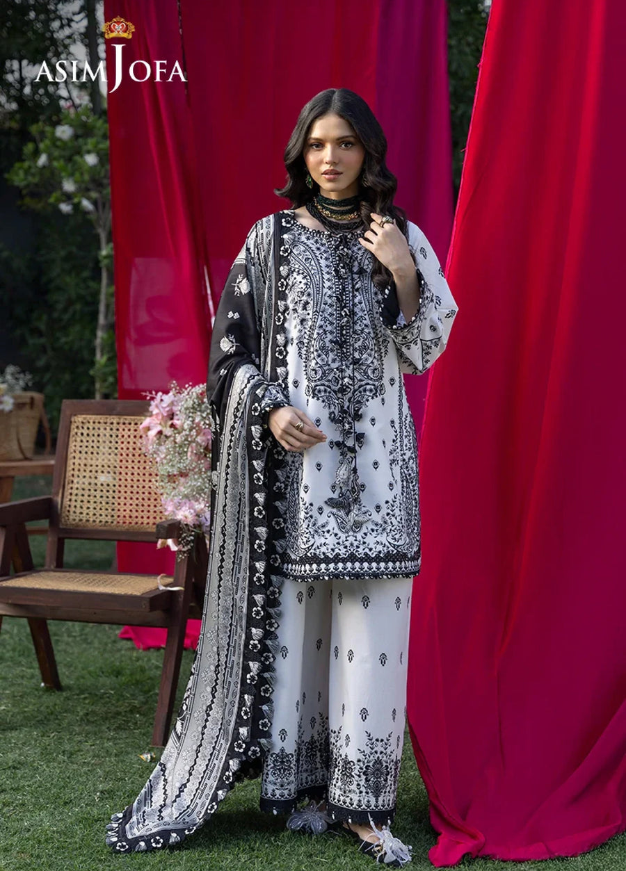 Woman wearing elegant black and white embroidered lawn suit with detailed floral and paisley embroidery, posing against a red backdrop.