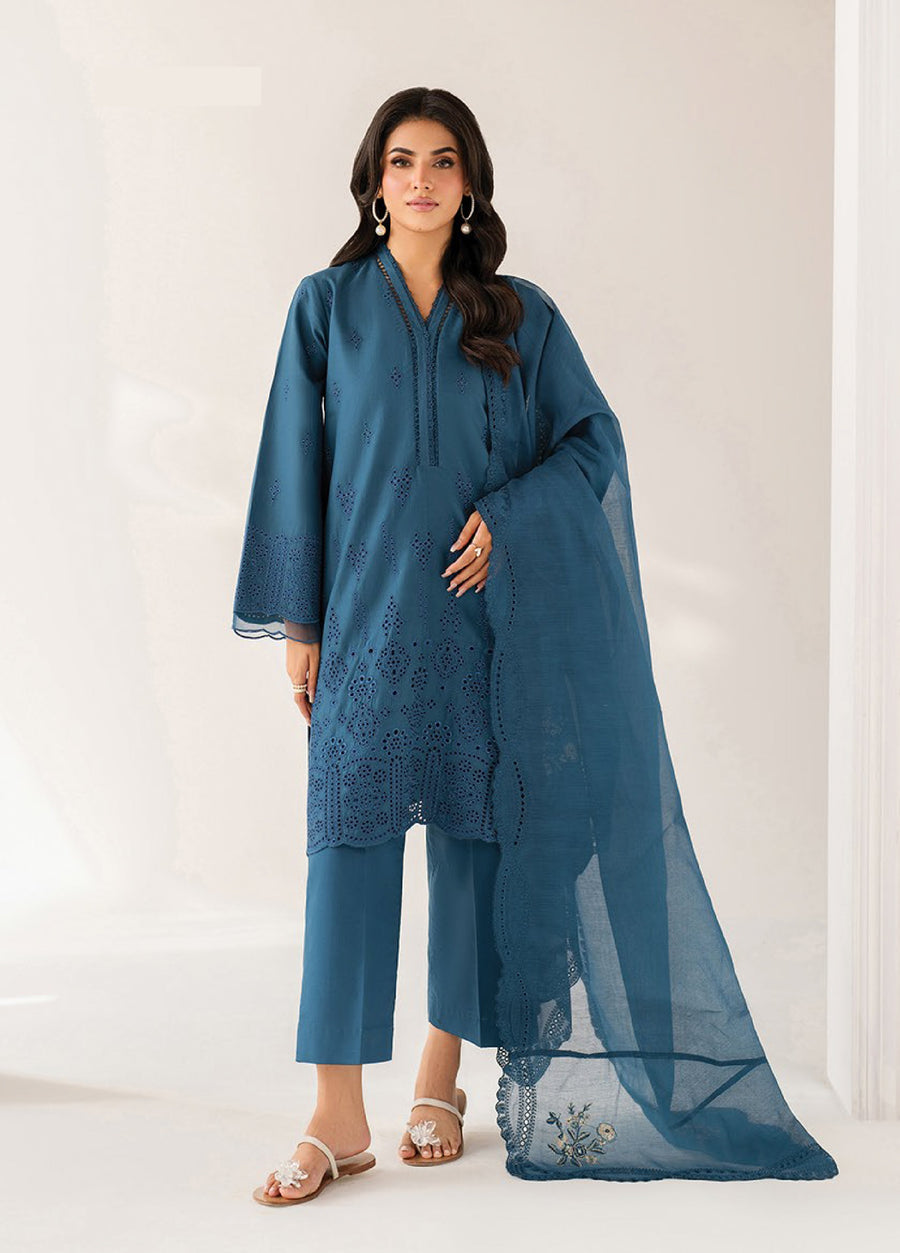 Woman standing wearing an elegant teal blue three-piece embroidered lawn suit with detailed cutwork on sleeves and hem, paired with a matching sheer dupatta and straight trousers