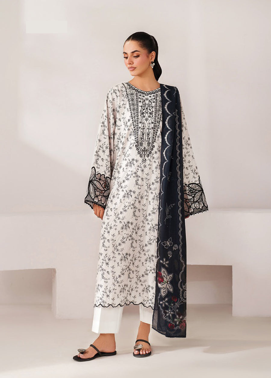 Woman standing wearing an off-white embroidered lawn shirt with floral black embroidery, paired with white trousers and a navy blue embroidered printed dupatta, styled with black sandals.