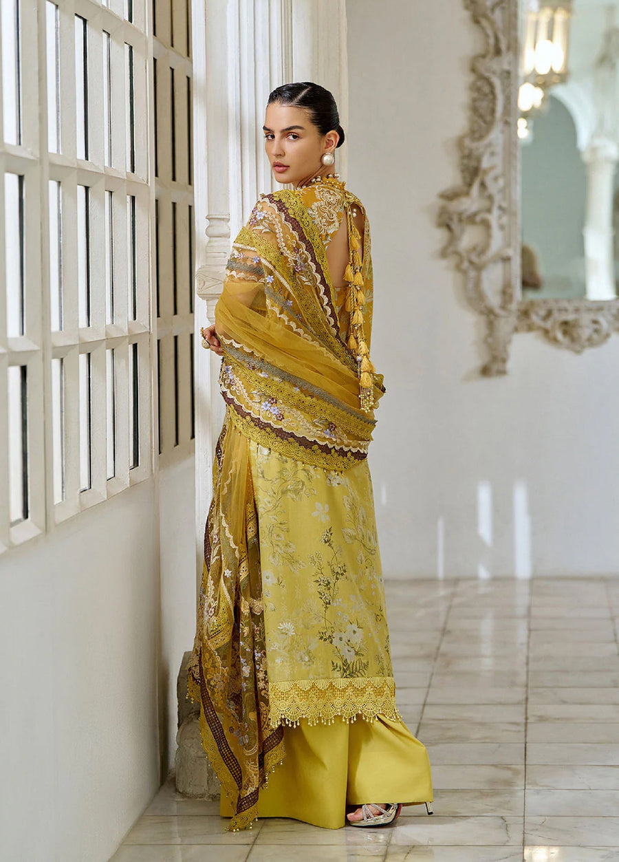 Back view of the same woman showing the open back design with tassel ties on the mustard embroidered lawn suit, along with the sheer dupatta draped over her shoulder and matching wide-leg pants.