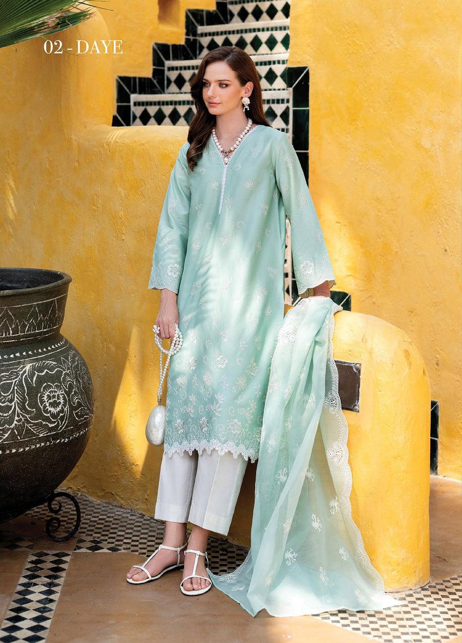 Woman wearing embroidered pastel green lawn suit holding matching dupatta, standing near yellow wall with black-and-white tiled stairs