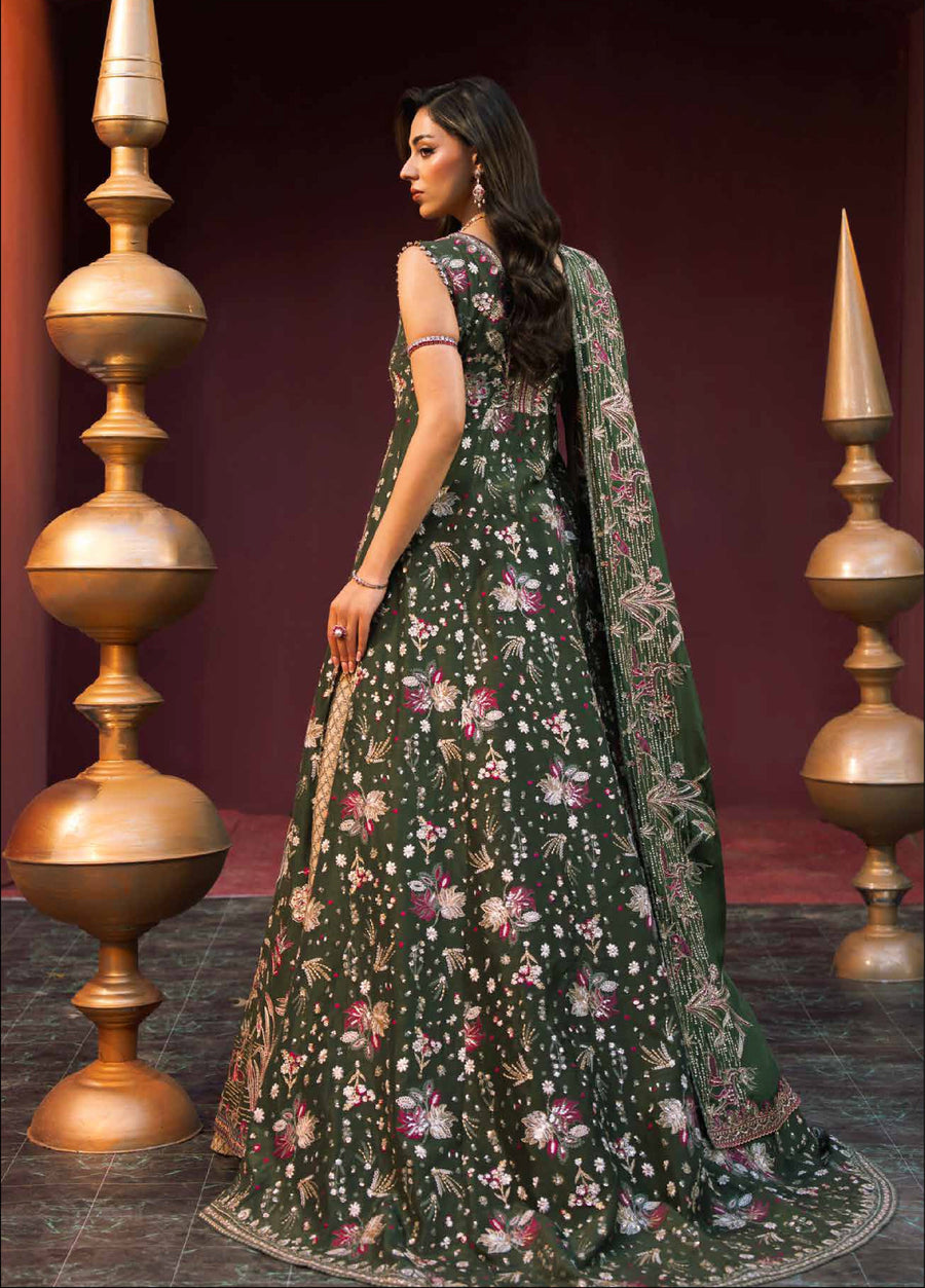 Back view of the same woman showcasing the intricately embroidered dark green long tunic with matching embroidered dupatta, paired with a golden lehenga skirt, standing between golden pillars.
