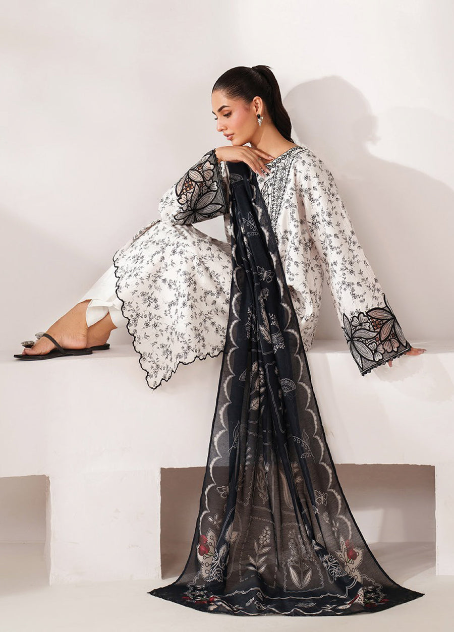 Woman seated in an off-white embroidered lawn suit with floral designs and black embroidery on the sleeves, holding a navy blue printed dupatta with floral and butterfly motifs.