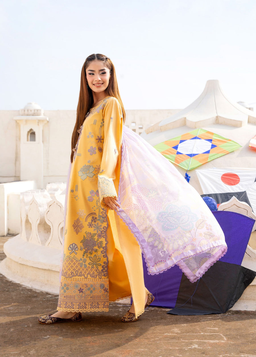 Side view of woman in mustard yellow embroidered suit holding flowing lavender printed chiffon dupatta with backdrop of white architecture and bright kites