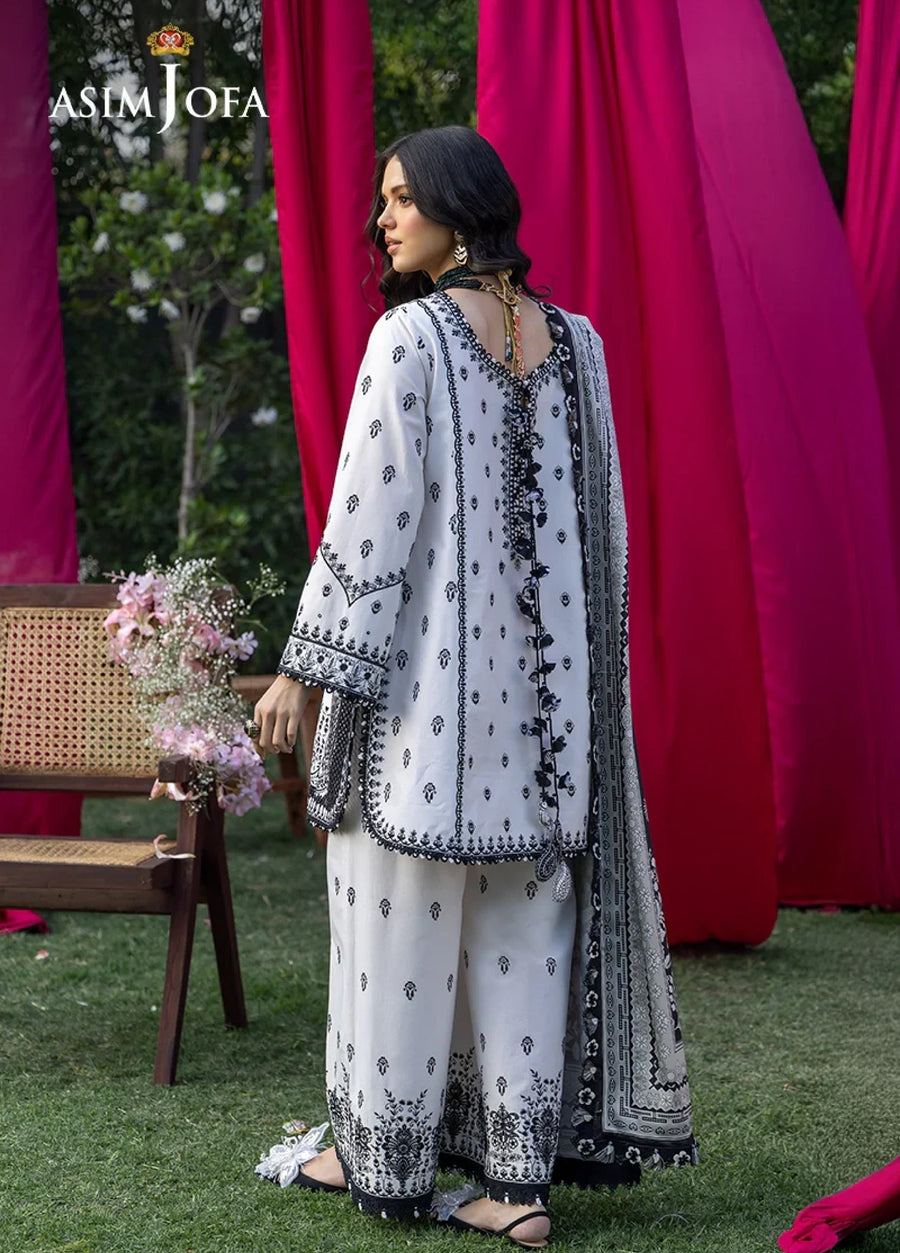 Back view of a woman in an embroidered black and white lawn suit showing intricate embroidery and tassel details on the tunic and trousers.