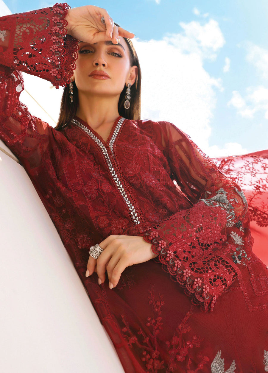 Portrait of a woman in a red embroidered lawn suit resting her arm, highlighting the delicate embroidery and lace details on the sleeve and neckline.