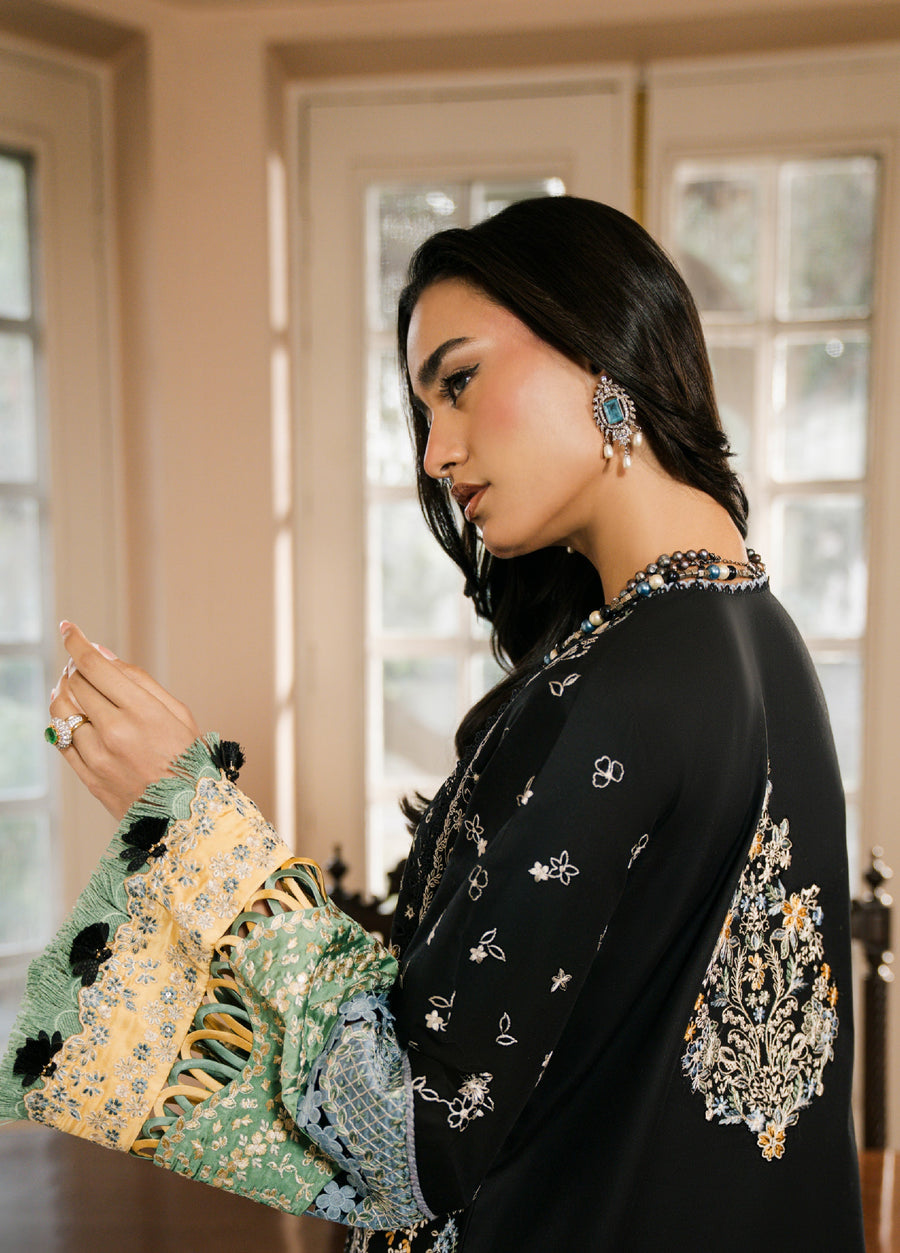 Close-up profile of woman wearing black embroidered suit highlighting intricate sleeve and back embroidery with matching jewelry