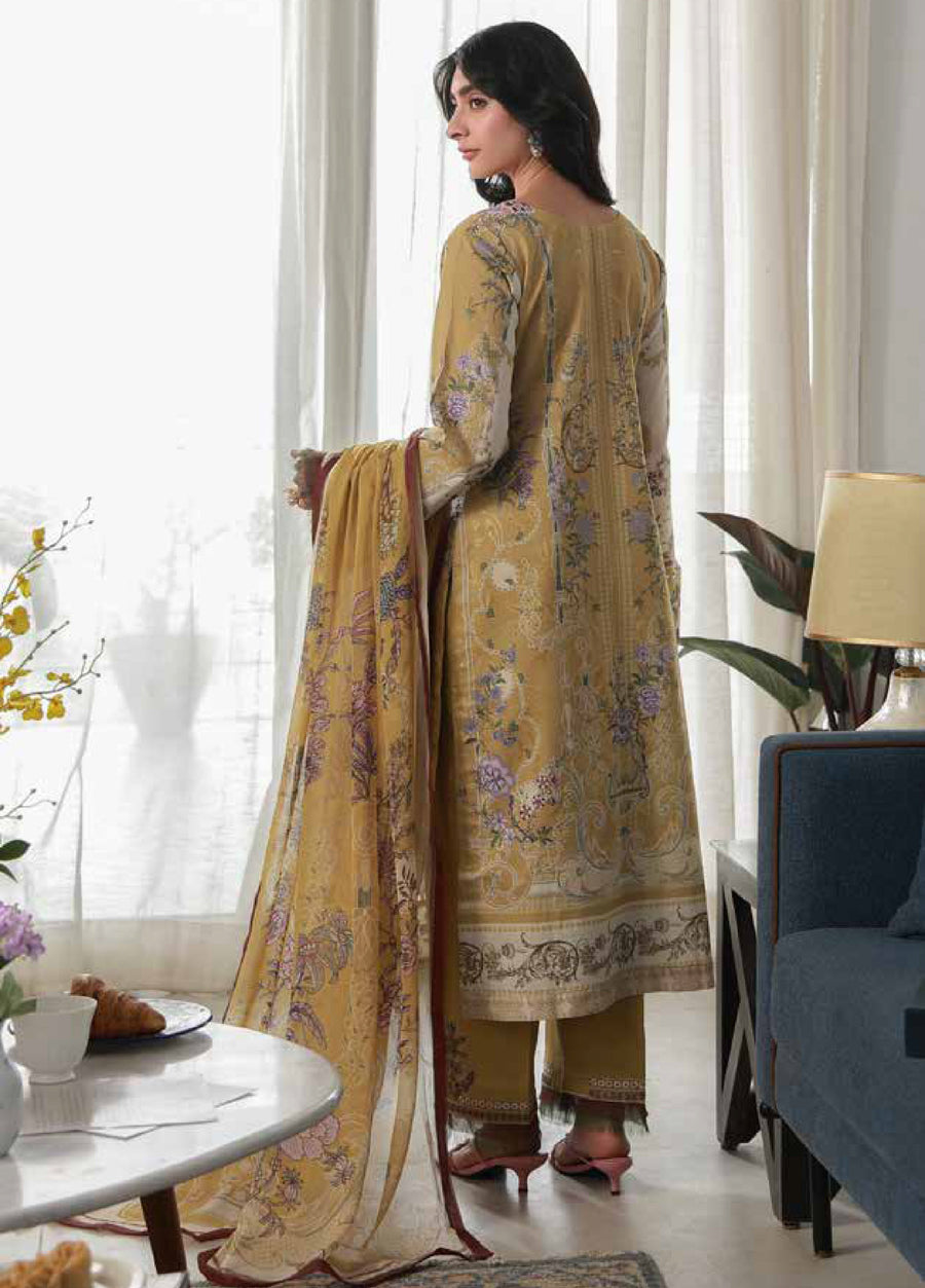 Back view of woman in mustard floral printed lawn shirt and trousers, holding matching printed chiffon dupatta, standing near blue sofa and lamp.