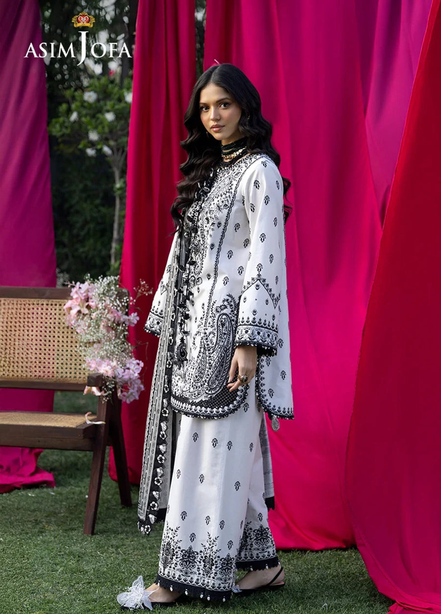 Side profile of woman in black and white embroidered lawn outfit showing delicate patterns and scalloped sleeves with tassels.
