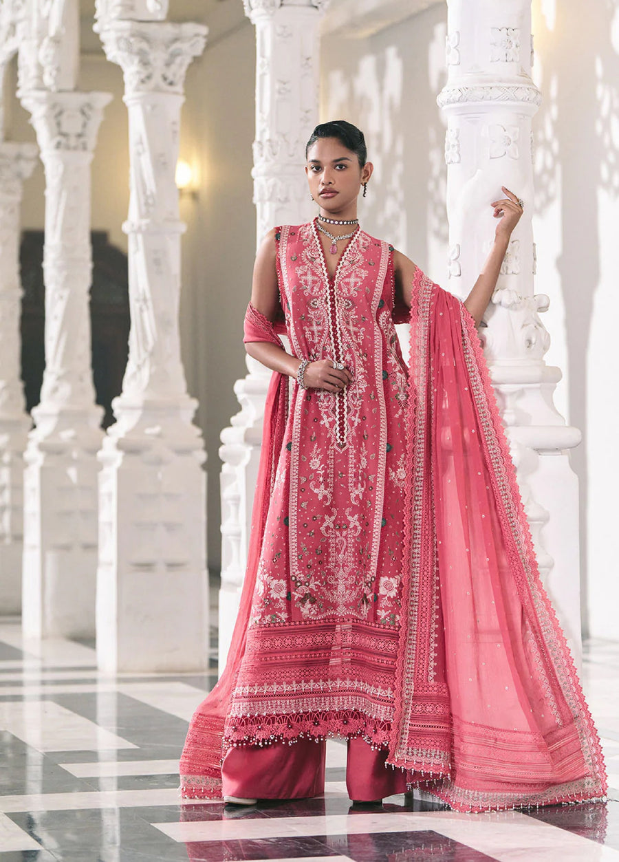 Woman showcasing pink embroidered lawn suit with detailed floral and geometric patterns, posing confidently near white pillar.