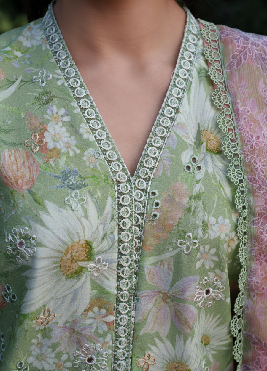 Close-up of the embroidered V-neckline with delicate circular lace trim and floral embroidery on pastel green fabric