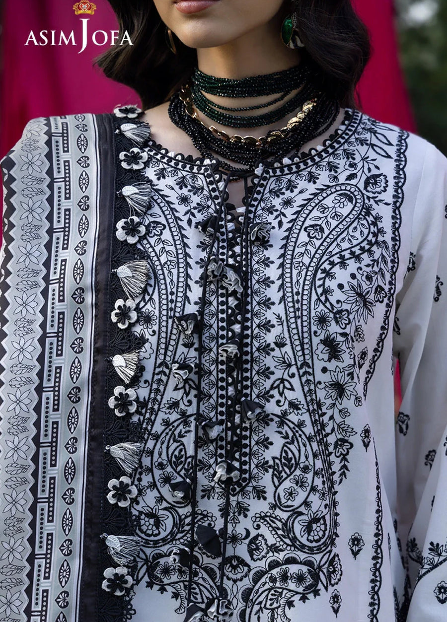 Close-up of detailed black floral and paisley embroidery with appliqué flowers and tassels on the front of white lawn fabric.