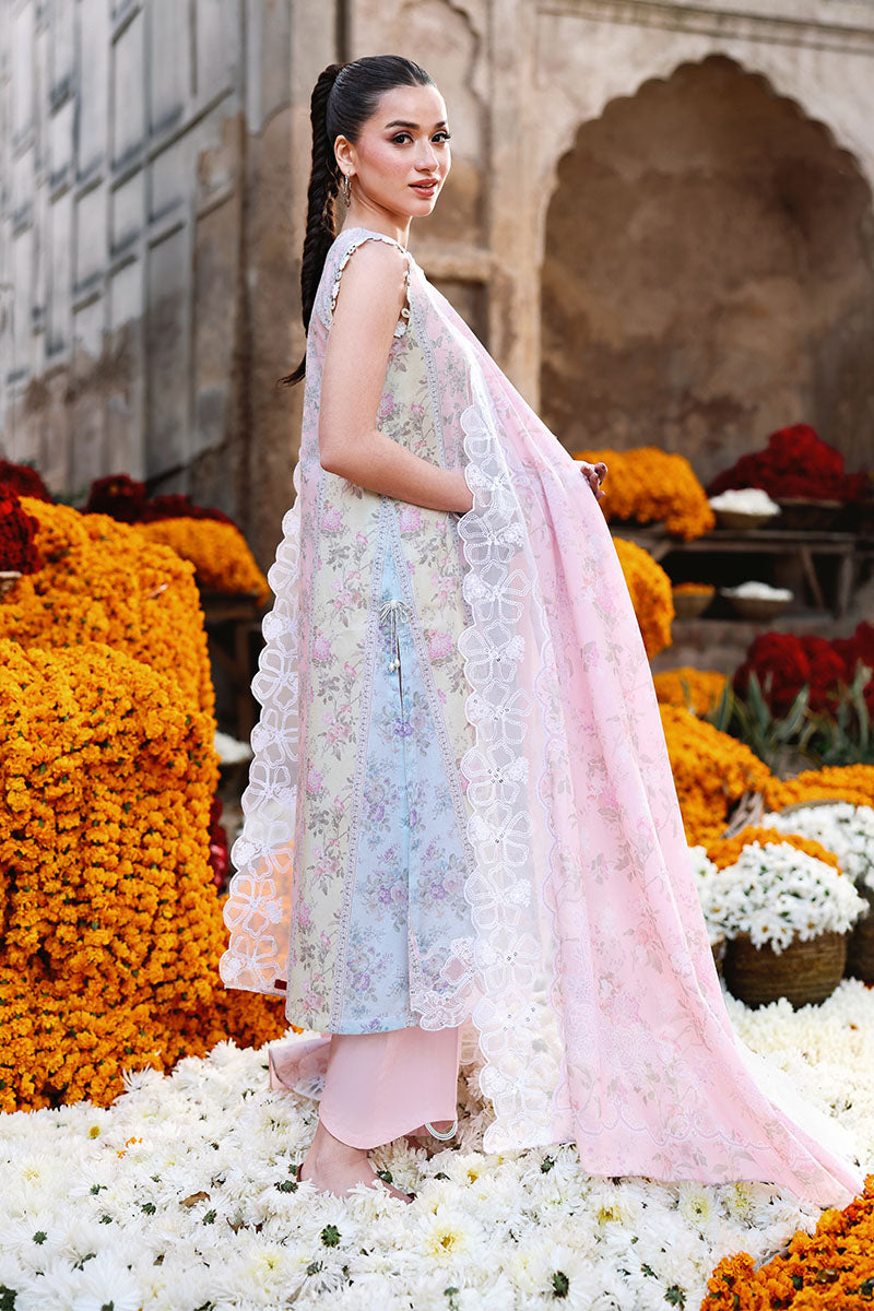 Side view of the woman wearing a pastel floral embroidered tunic and holding the embroidered dupatta draped over her shoulders, surrounded by marigold flowers.