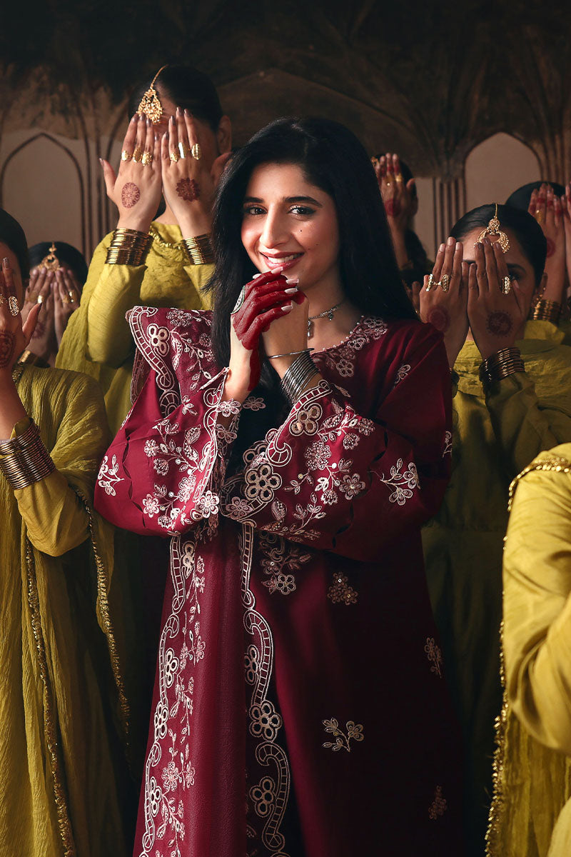 Woman in embroidered crimson lawn suit smiling with henna on hand, presenting detailed embroidery on sleeves and front