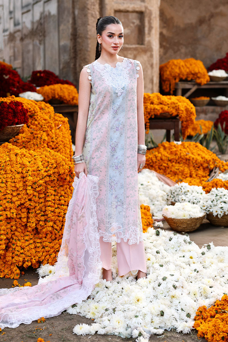 Woman wearing a sleeveless floral embroidered pastel pink and blue lawn tunic with matching pink trousers, standing amidst vibrant orange and white marigold flowers.