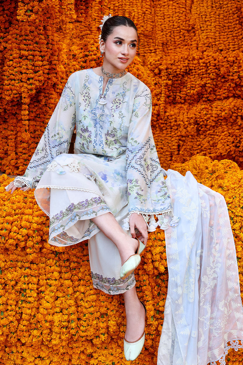 Woman sitting poses to show detailed embroidery on lawn shirt and trousers with delicate tassels and pastel blue dupatta