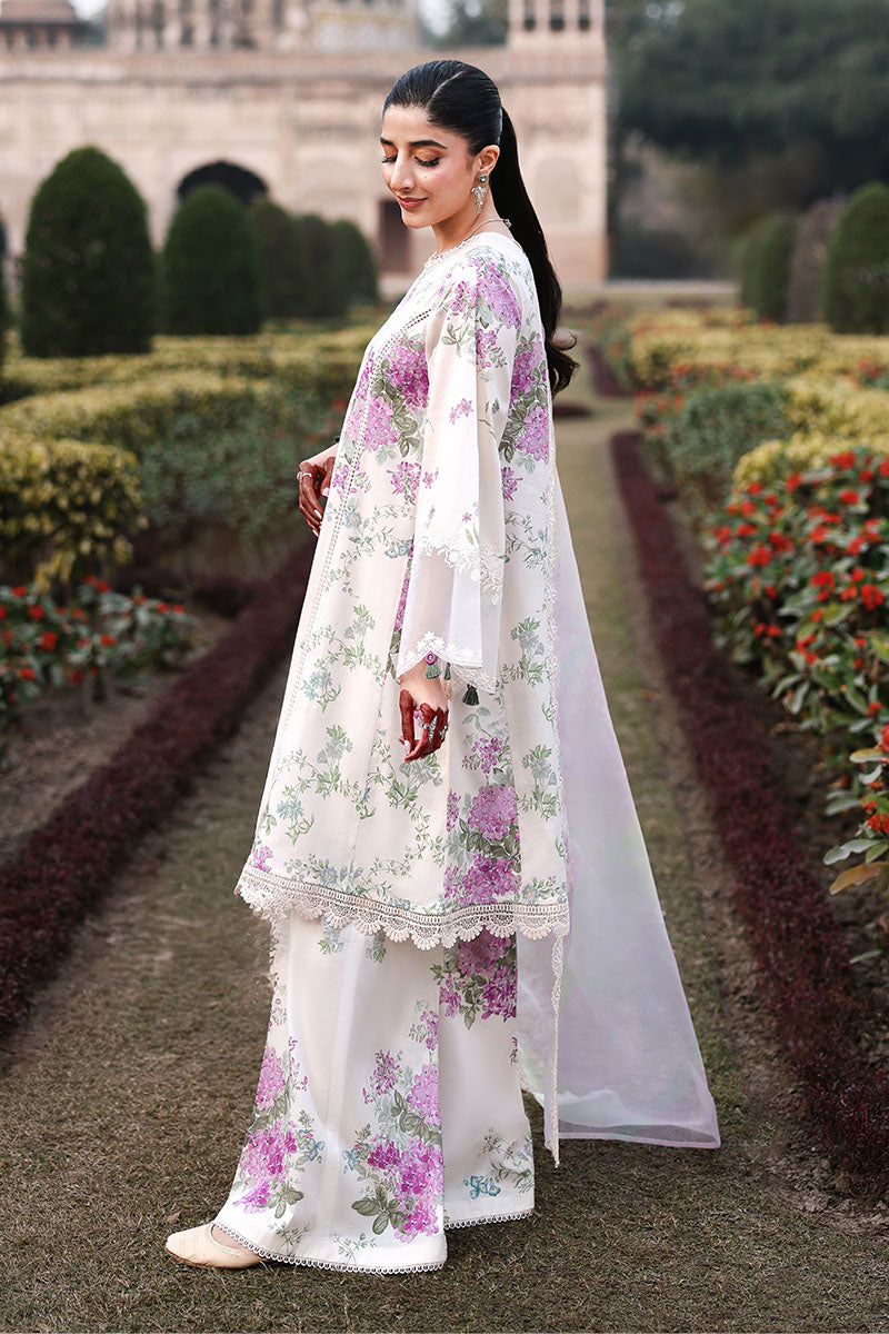 Side profile of woman wearing the cream and floral three-piece lawn suit standing in a garden, showing the wide-leg pants and flowing sheer dupatta.
