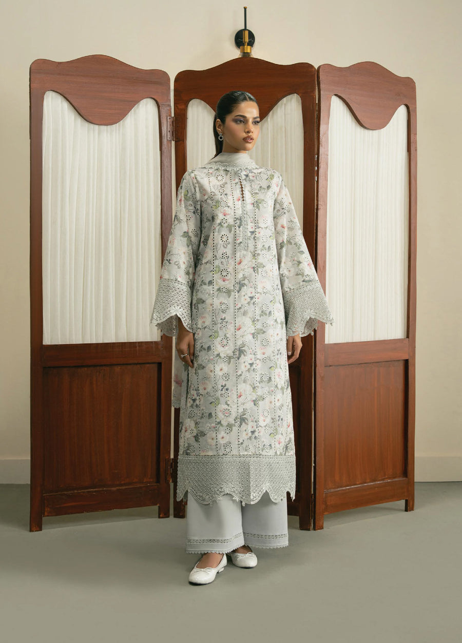 Front view of a woman wearing an elegant light gray floral embroidered suit with scalloped eyelet lace on sleeves and hem, paired with matching wide-leg trousers and white shoes standing in front of a wooden folding screen.