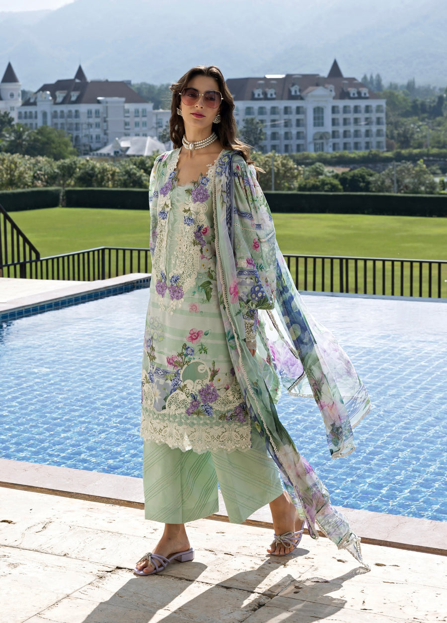 Woman wearing a pastel green embroidered lawn suit with floral patterns, sheer chiffon dupatta flowing, standing beside a pool with elegant background