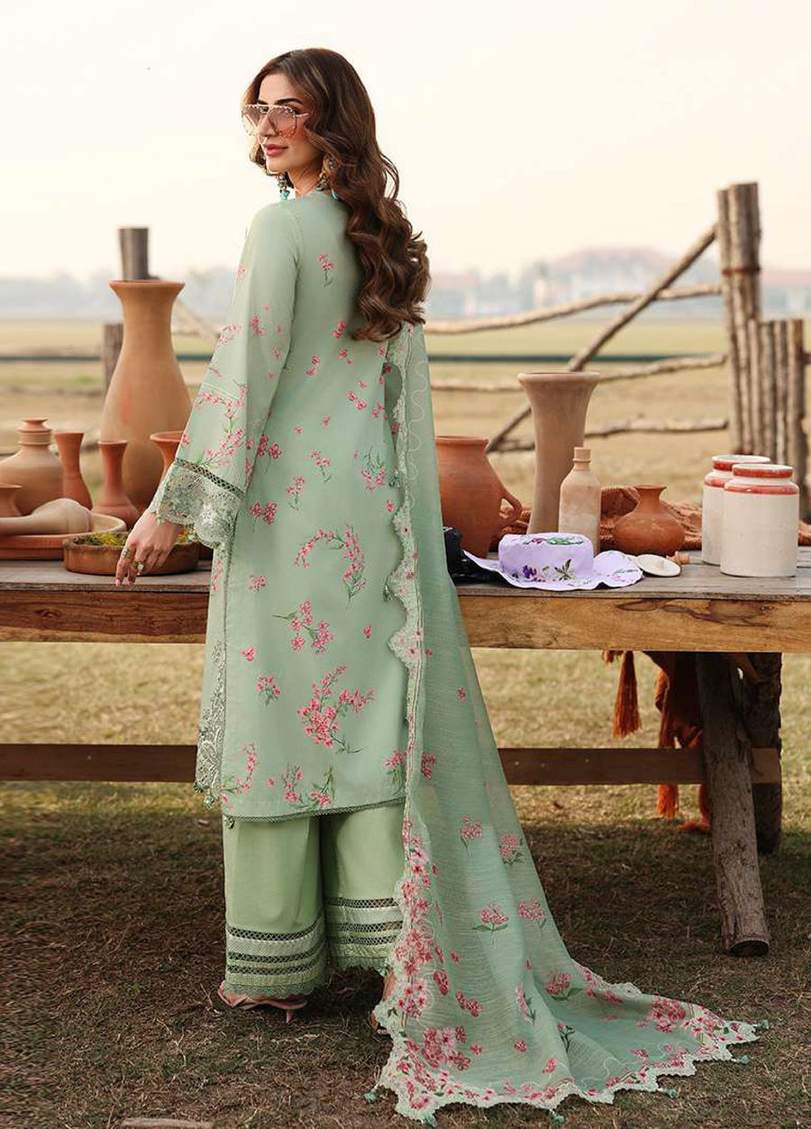 Back view of a woman dressed in a pastel green embroidered suit featuring floral designs and a scalloped dupatta near a rustic wooden table.