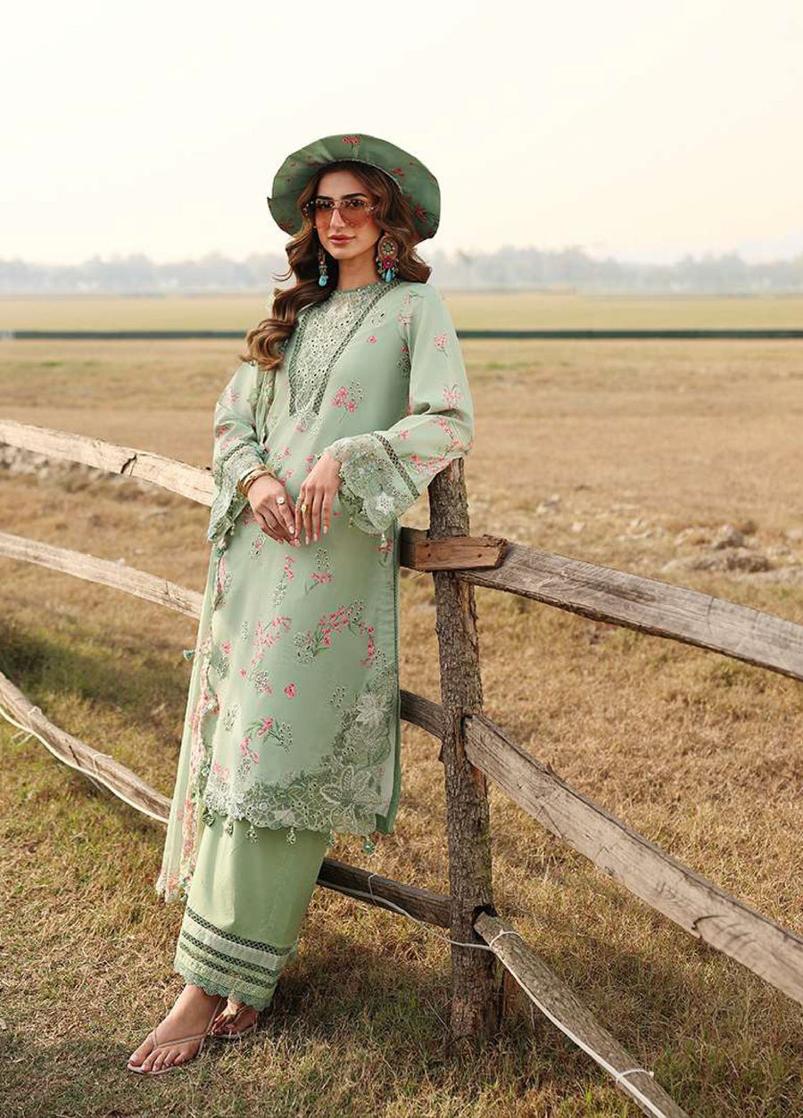 Woman in an embroidered lawn suit leaning against a wooden fence in an open field, accessorized with statement earrings and sunglasses.