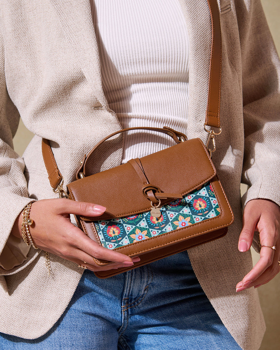 Woman holding a brown leather crossbody bag with embroidered floral design, wearing a beige blazer and blue jeans