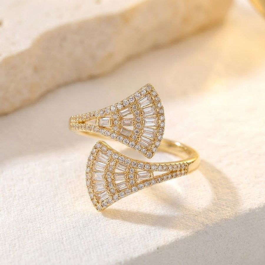 Gold fan-shaped ring placed on light textured surface highlighting sparkling stones and fan design