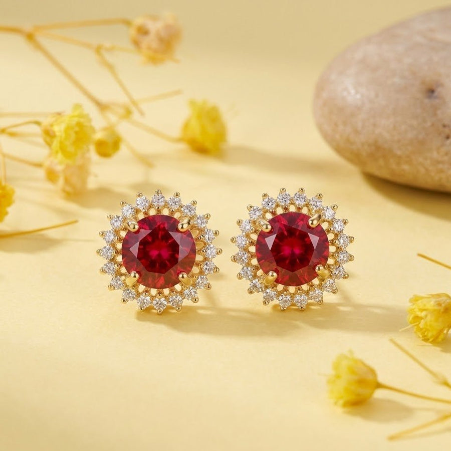 Red gemstone halo stud earrings arranged on a yellow surface with dried flowers