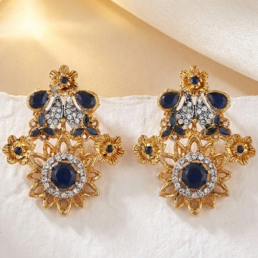 Royal blue flower-shaped gemstone earrings with sparkling accents on soft white fabric background