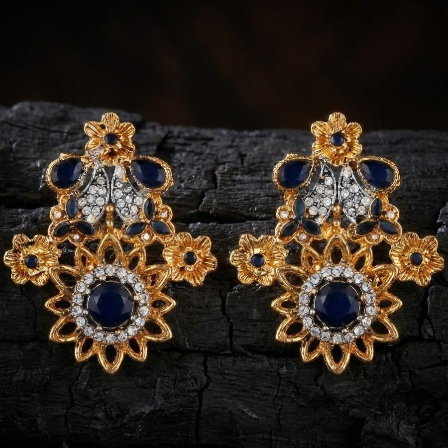 Close view of royal blue floral earrings resting on textured dark surface under warm lighting